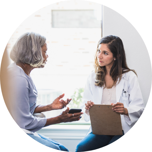 An image of a female provider holding a clipboard while talking with an elderly patient holding a phone.